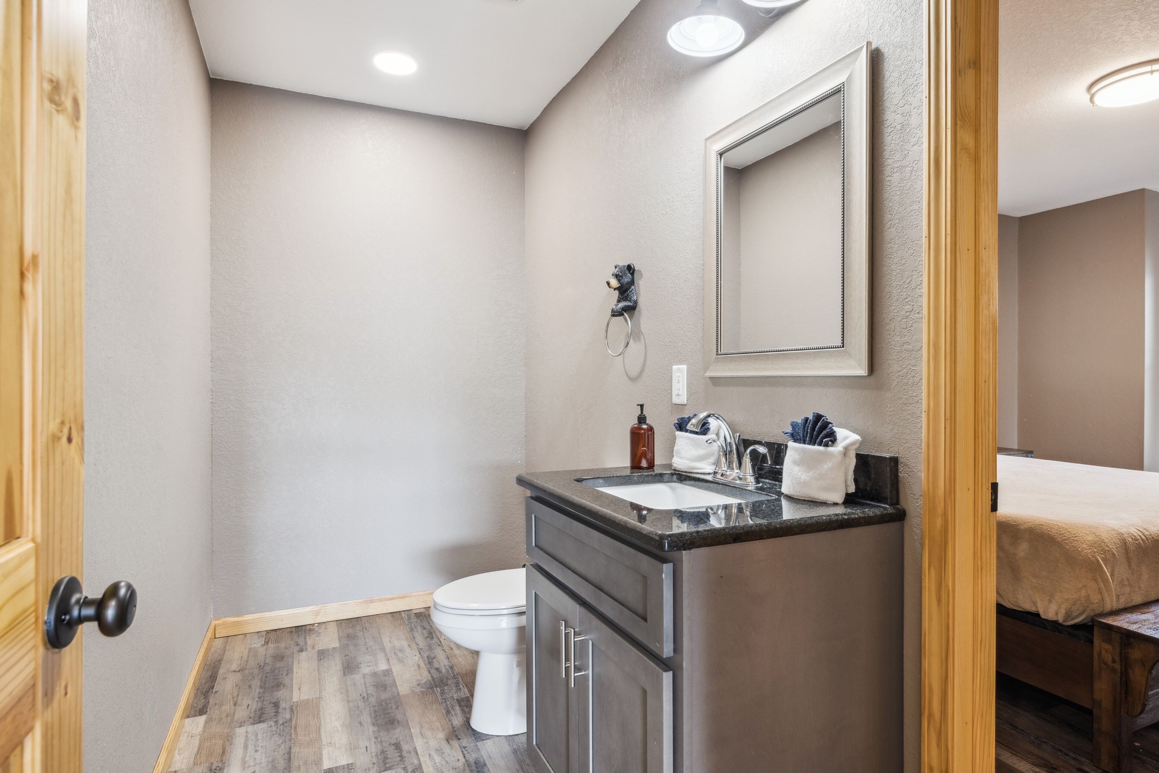 A compact bathroom with a toilet, a sink with a mirror, and a wooden floor.