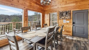A wooden cabin with a dining area featuring a table and chairs, large windows, and a gray door. - Wild Heart Lodge 4 Bedroom Cabin (Sevierville)