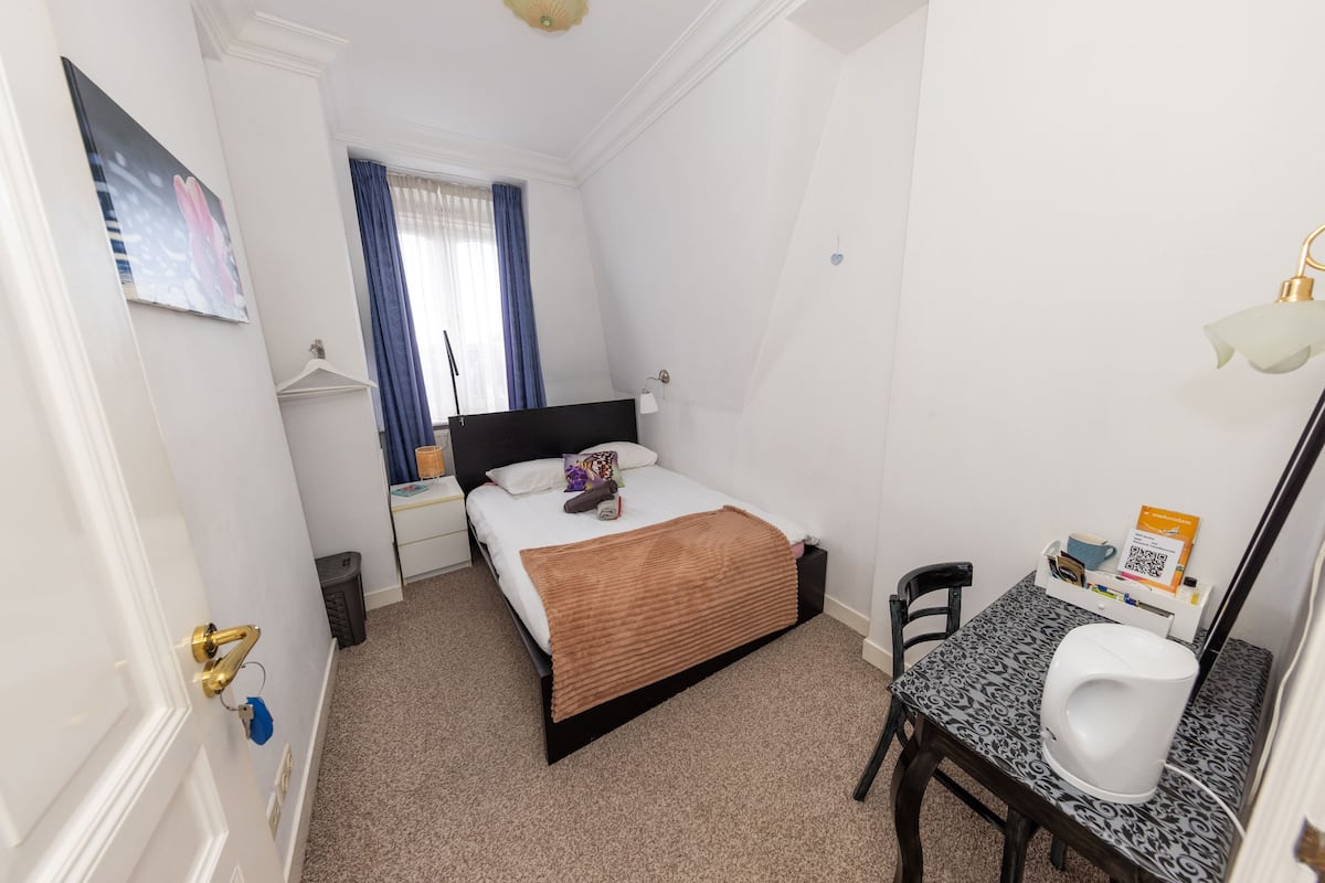 A small, clean room with a bed, bedside table, and a desk with a chair.