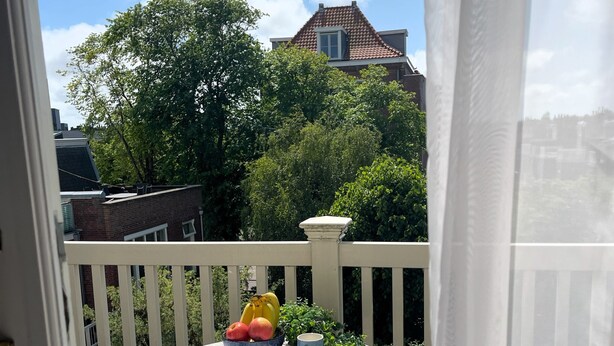 A balcony with a table set for two, a bowl of fruit, and a book. - Flora's Palace (The Hague)