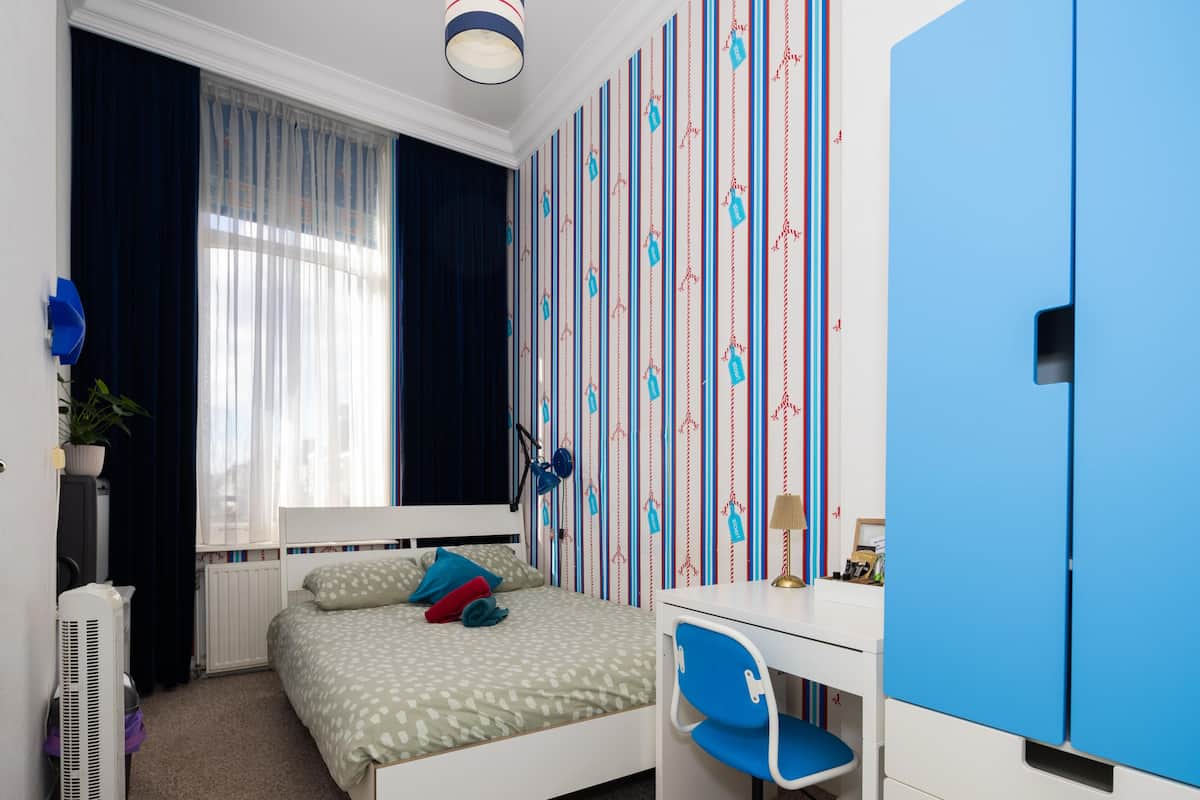 A bedroom with a bed, a desk, and a wardrobe.