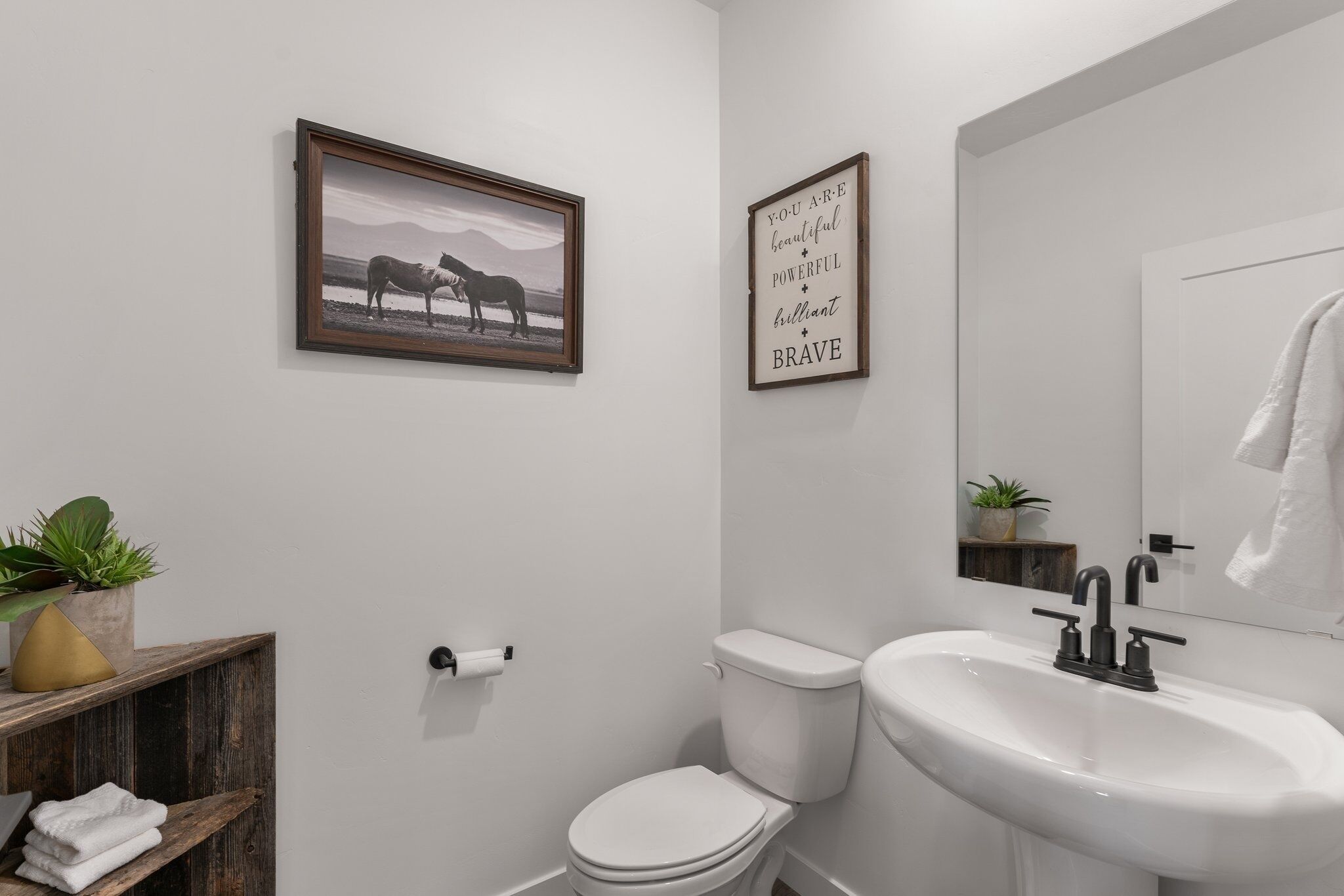 A bathroom with a toilet, sink, and framed pictures on the wall.