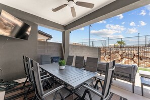 Un patio al aire libre con una mesa y sillas, un ventilador de techo y vistas del paisaje circundante.