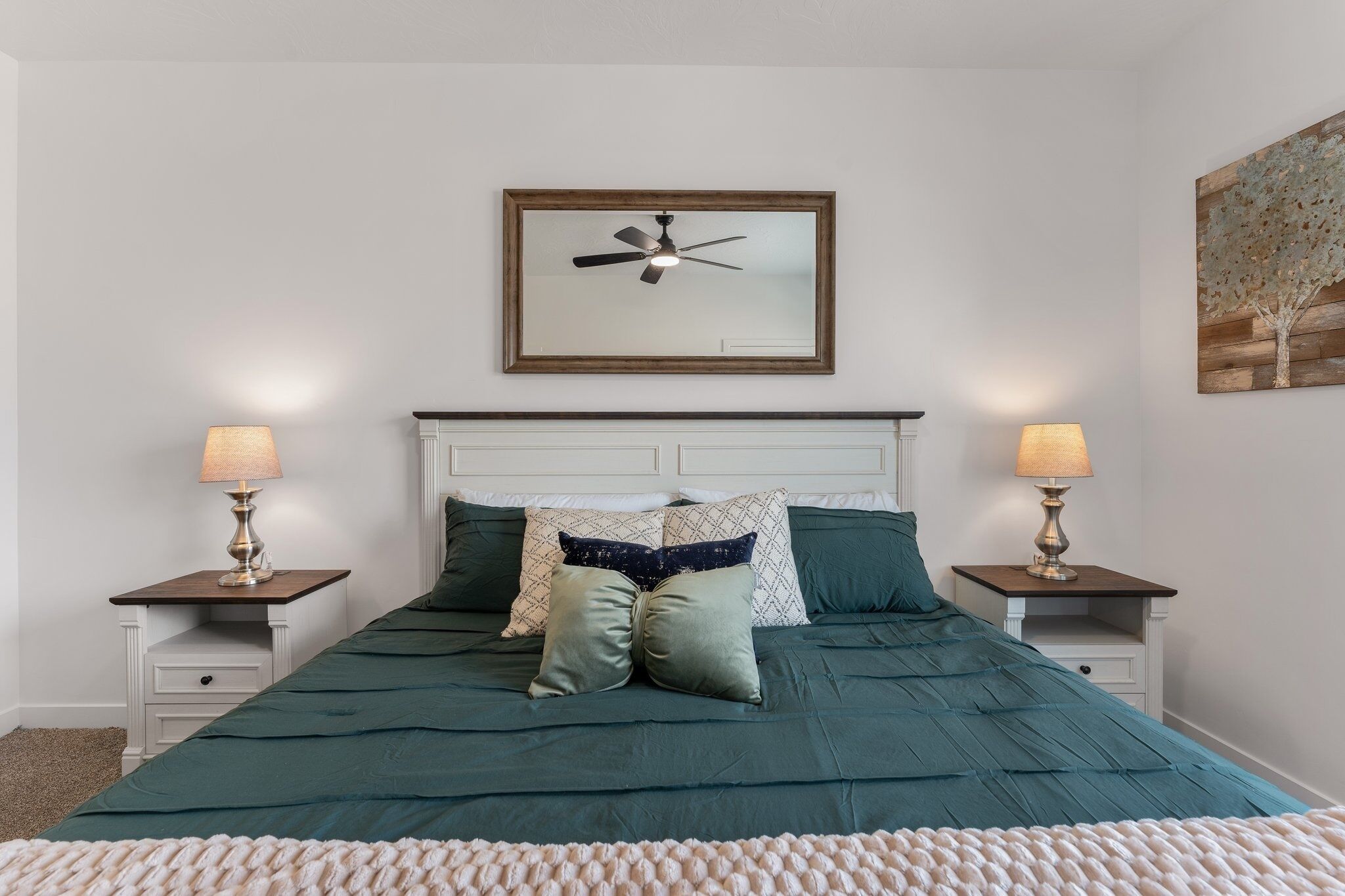 A bedroom with a bed, two bedside tables, a ceiling fan, and a wall-mounted painting.