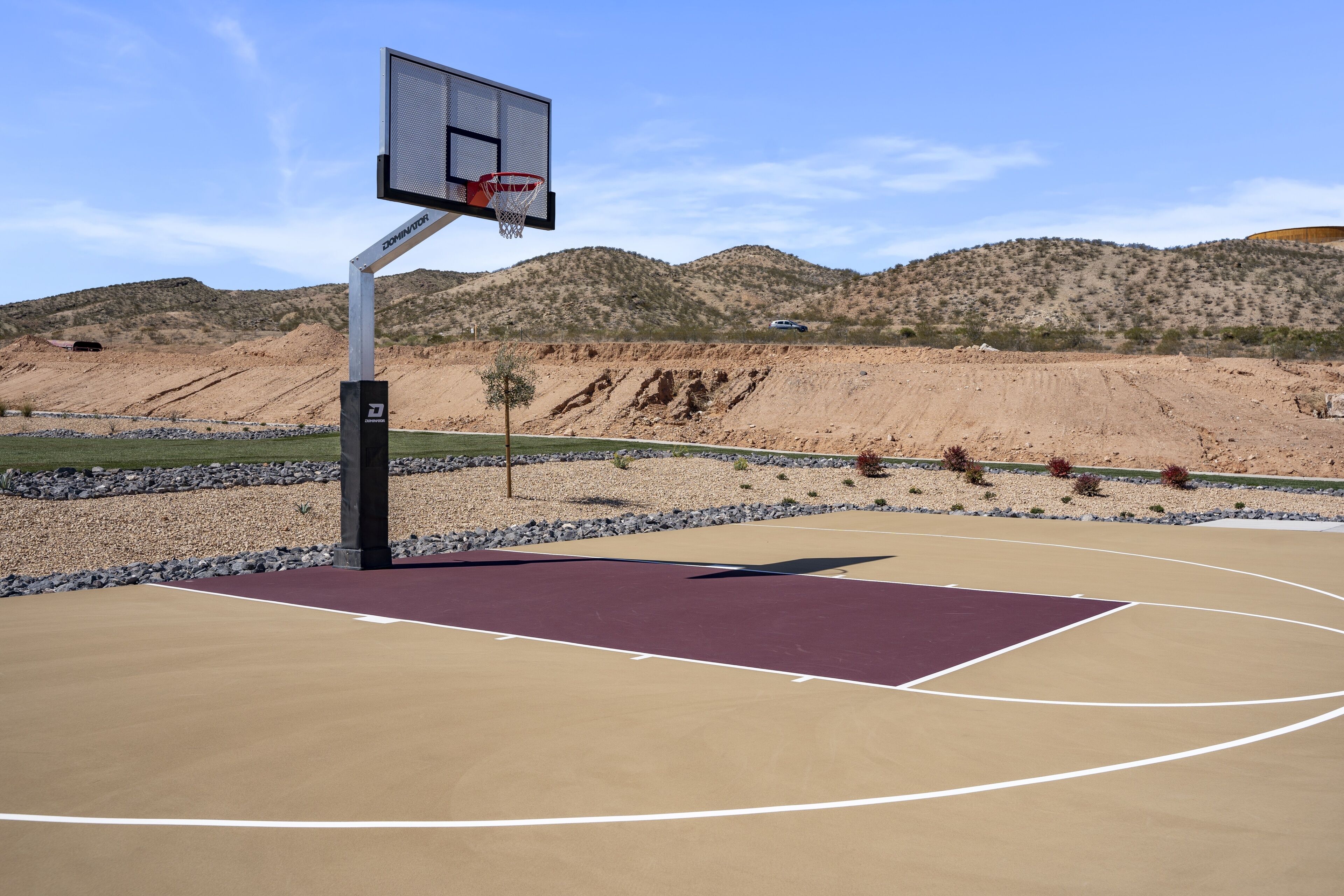 An outdoor basketball court with a metal basketball hoop and a clear view of a mountainous landscape in the background.