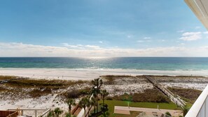 Une vue sur la plage depuis un balcon doté d’une terrasse en bois et bordé de palmiers.