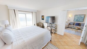 A hotel room with a large bed, a desk with a flat-screen TV, a sofa, and a painting on the wall.