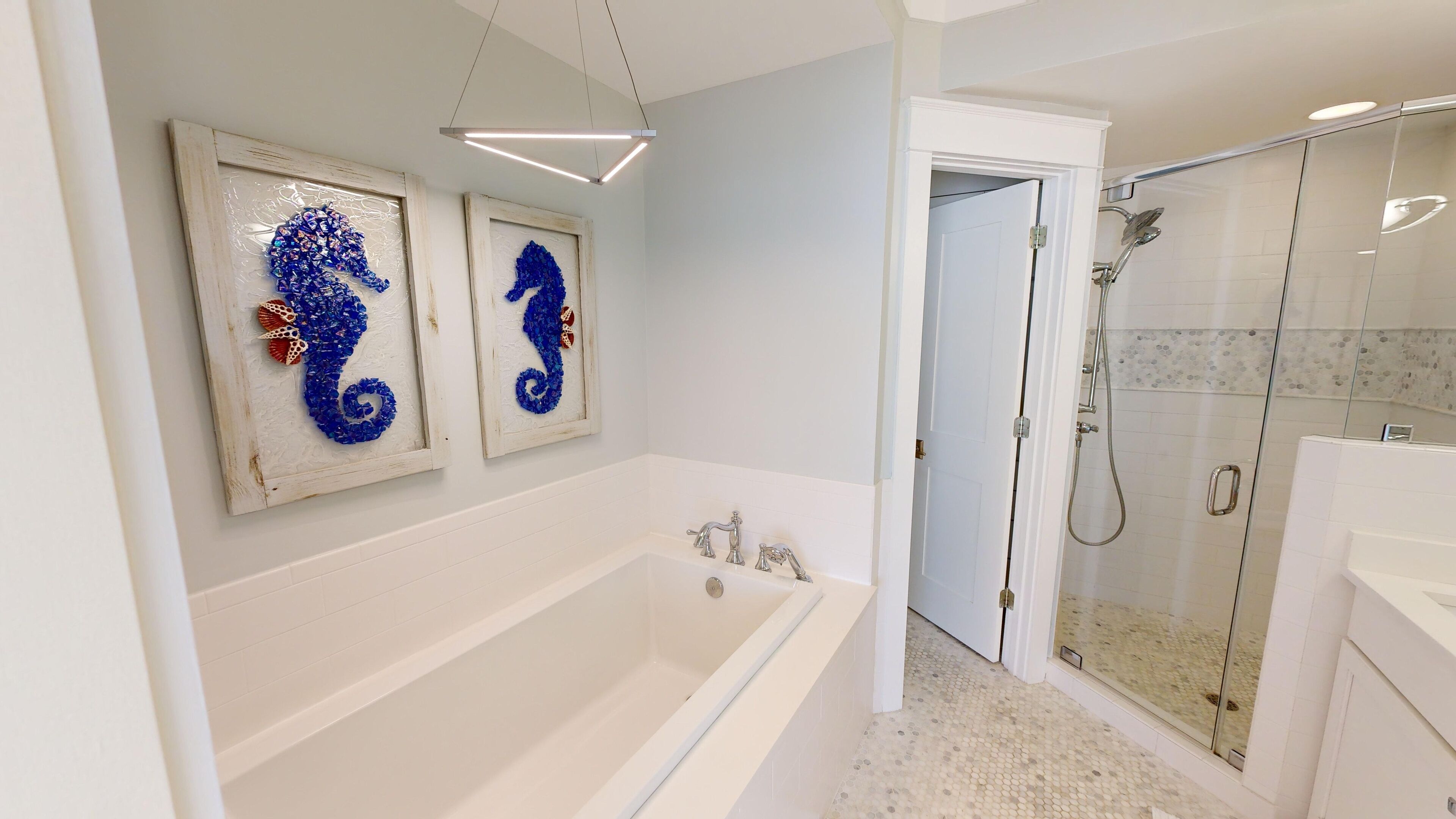 Een moderne badkamer met een vrijstaand bad, een douche met glazen wand en twee afbeeldingen van paardenzeepaardjes in lijsten aan de muur.