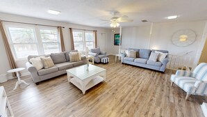 Un salon spacieux avec un canapé gris, un canapé bleu, un fauteuil à rayures et une table basse en verre.