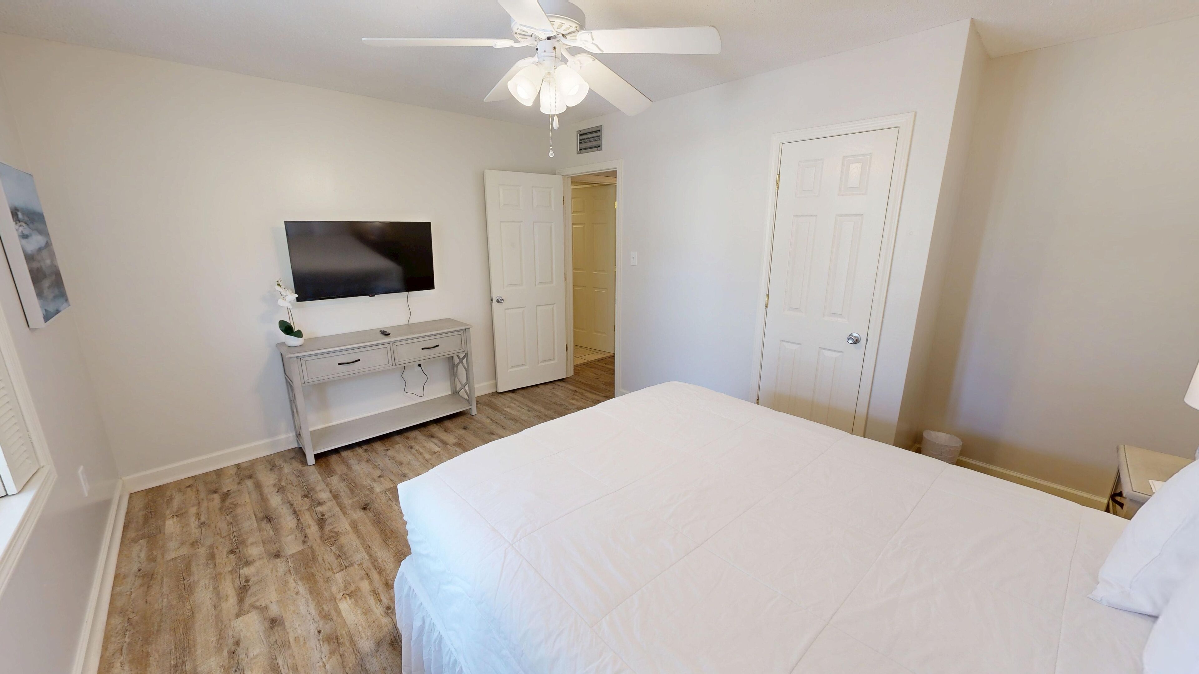 A bedroom with a bed, a dresser, a television, and a ceiling fan.