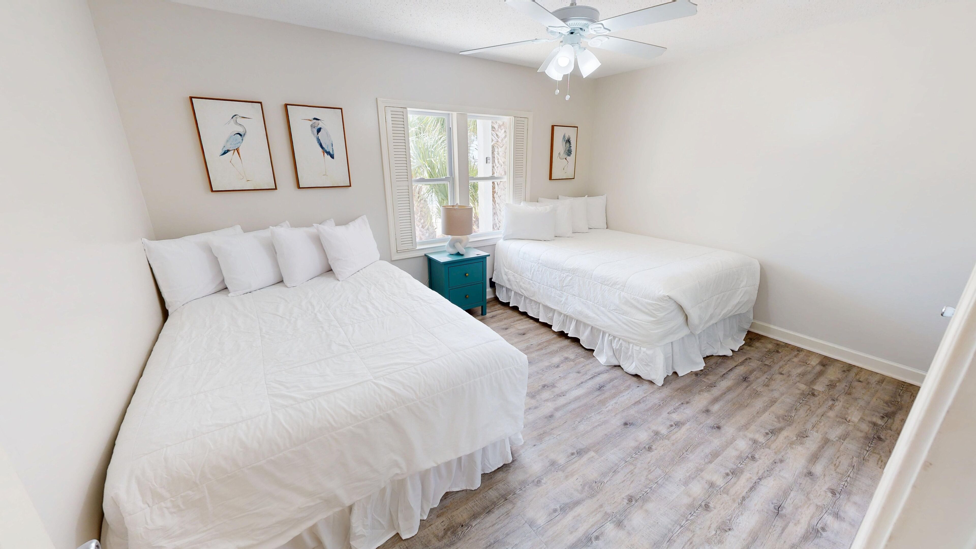 A bedroom with two beds, a ceiling fan, and artwork on the walls.