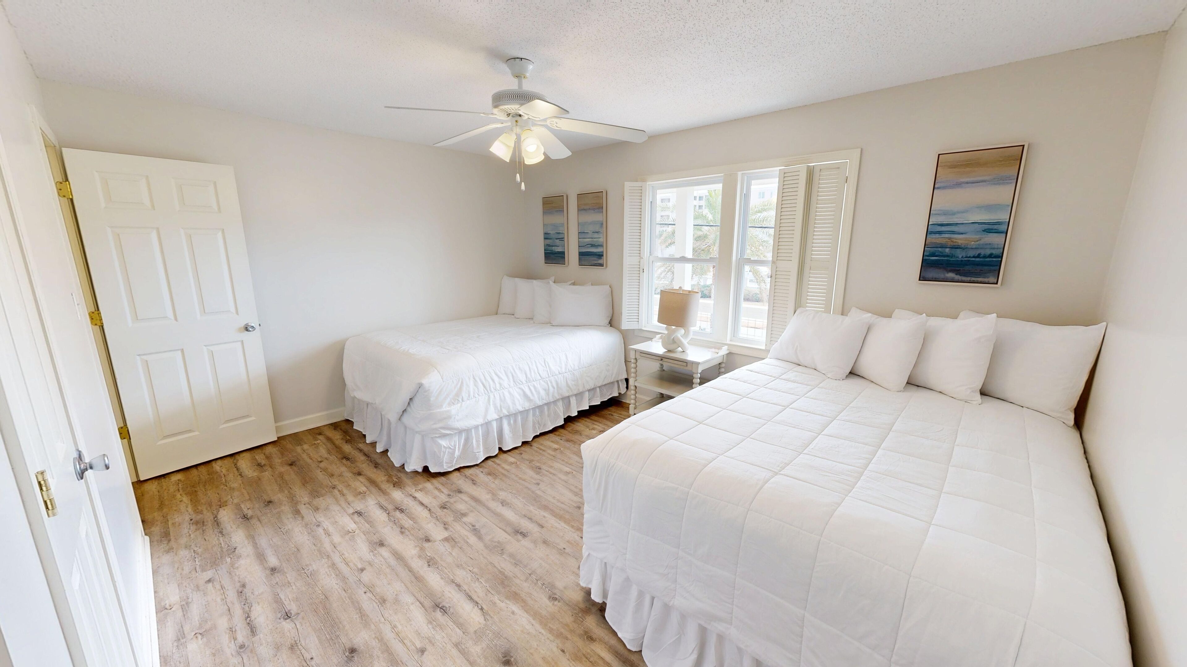 A bedroom with two beds, a ceiling fan, and a window with shutters.