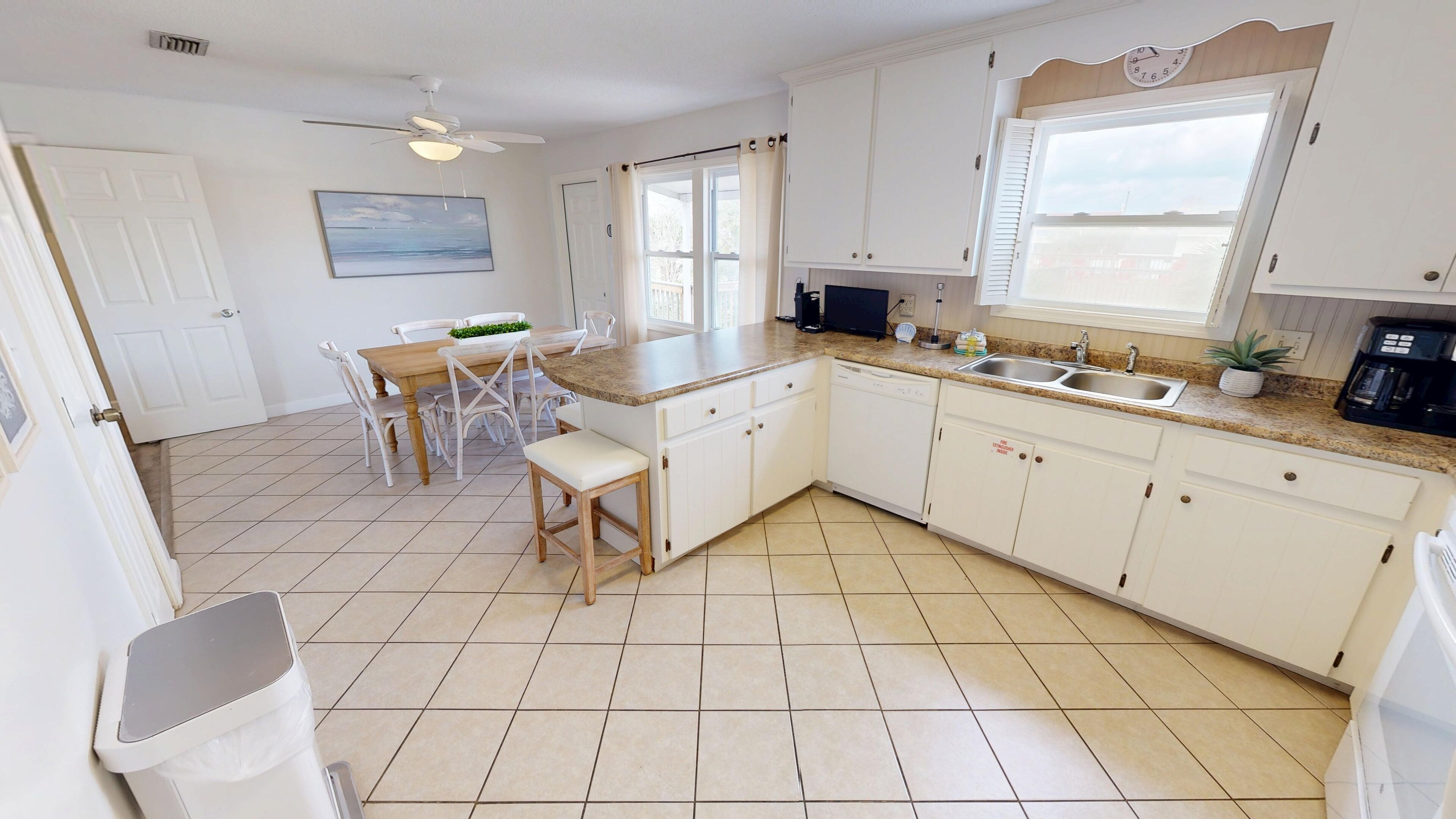 A kitchen with white cabinets, a granite countertop, a dishwasher, and a dining area with a table and chairs.