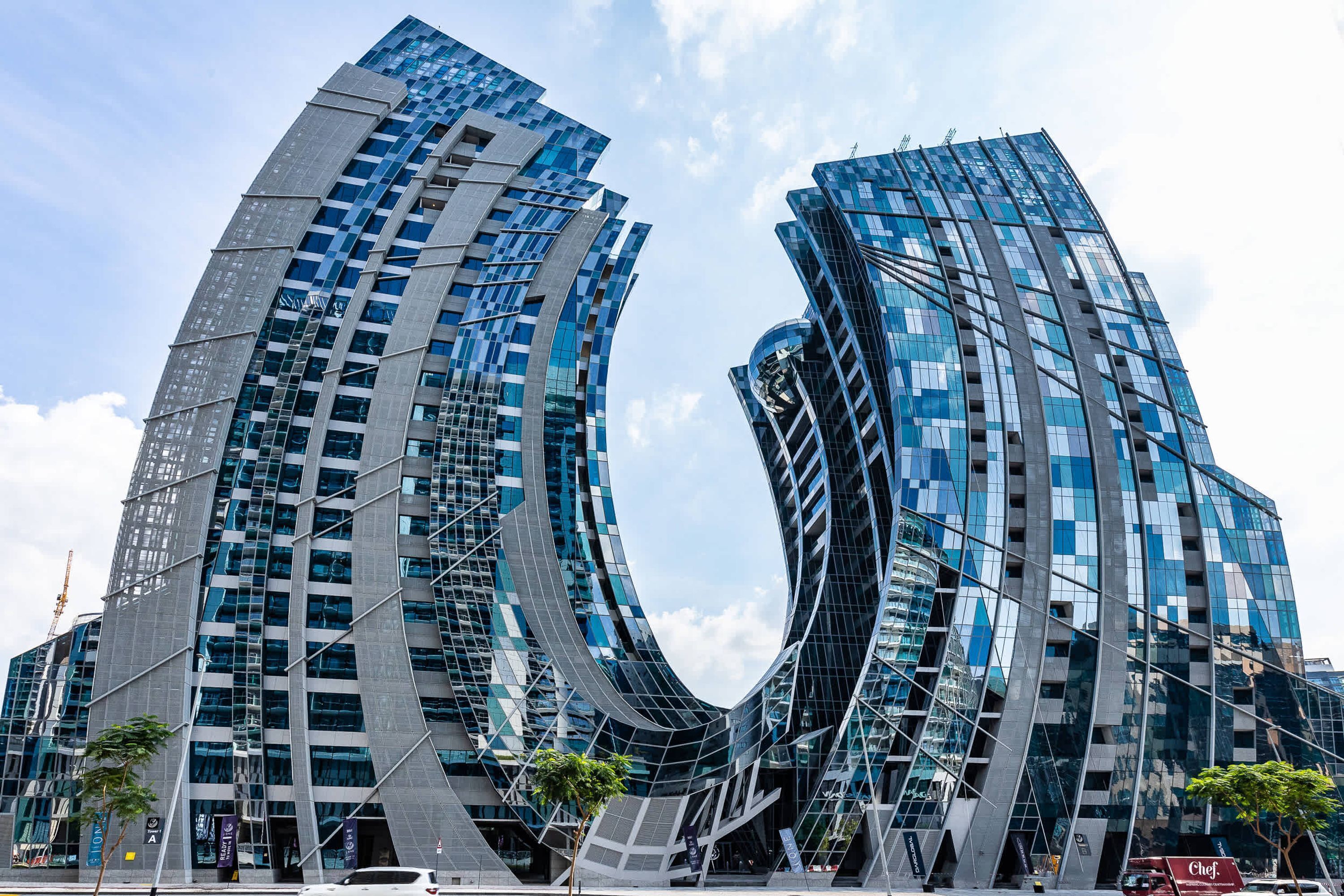 Ein modernes Gebäude mit einem markanten, geschwungenen Design, das zahlreiche Glasfenster und eine reflektierende Fassade aufweist.