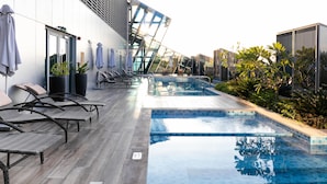 Un área de piscina moderna al aire libre con sillones de descanso y una zona de estar con paredes de cristal.