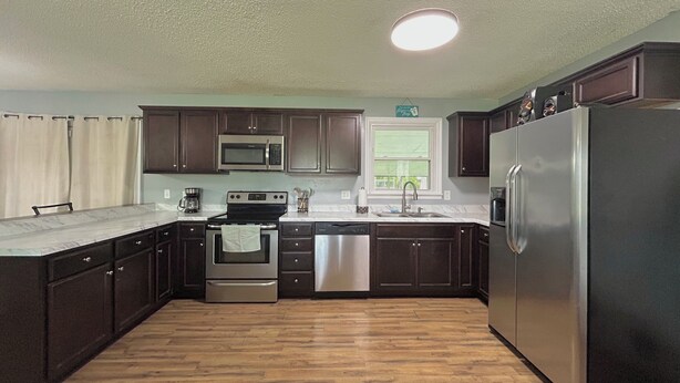 A kitchen with dark wooden cabinets, stainless steel appliances, a window, and a wooden floor.