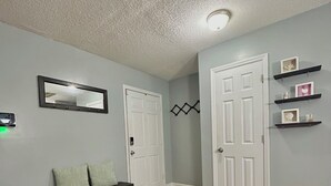 A hallway with wooden flooring, a bench with storage drawers, two white doors, a wall-mounted mirror, and a ceiling light fixture.