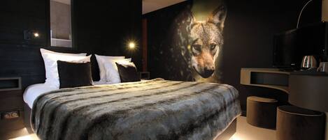 Un dormitorio moderno con una cama grande, televisión y un mural de un lobo en la pared.