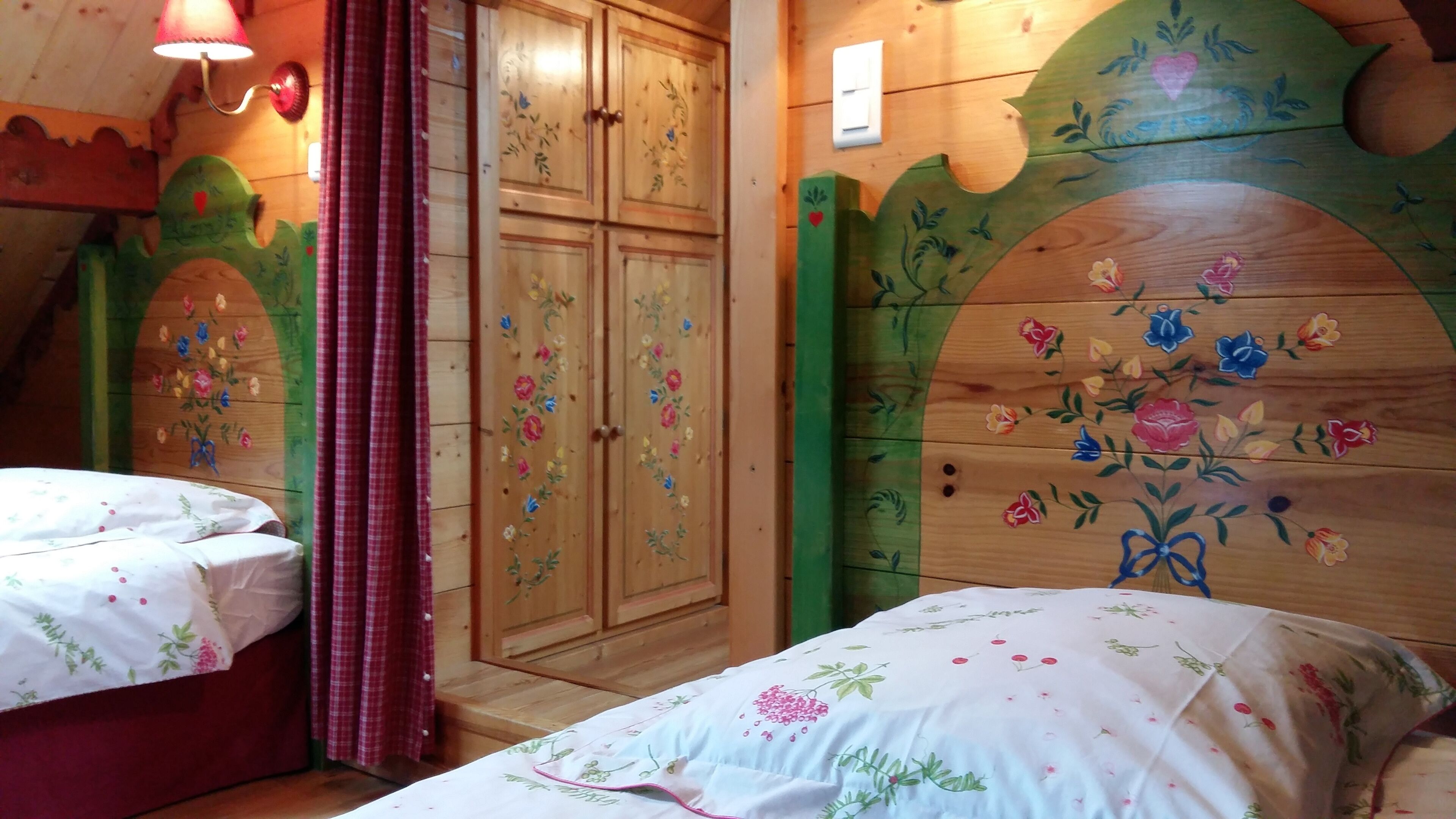 A room with two beds, wooden walls, floral decorations, and a checkered curtain.