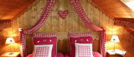Een gezellige kamer met een houten plafond, twee bedden met rood-wit geruit beddengoed, hartvormige kussens en passende gordijnen.