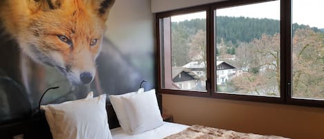 Ein Schlafzimmer mit großem Fenster, einem Bett mit weißen Kissen und einer Wandmalerei eines Fuchses.
