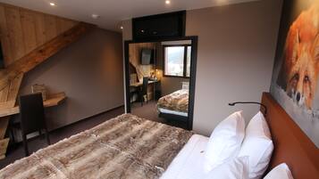 Une chambre avec un grand lit, un bureau en bois, une chaise, un téléviseur fixé au mur et un tableau représentant un renard.
