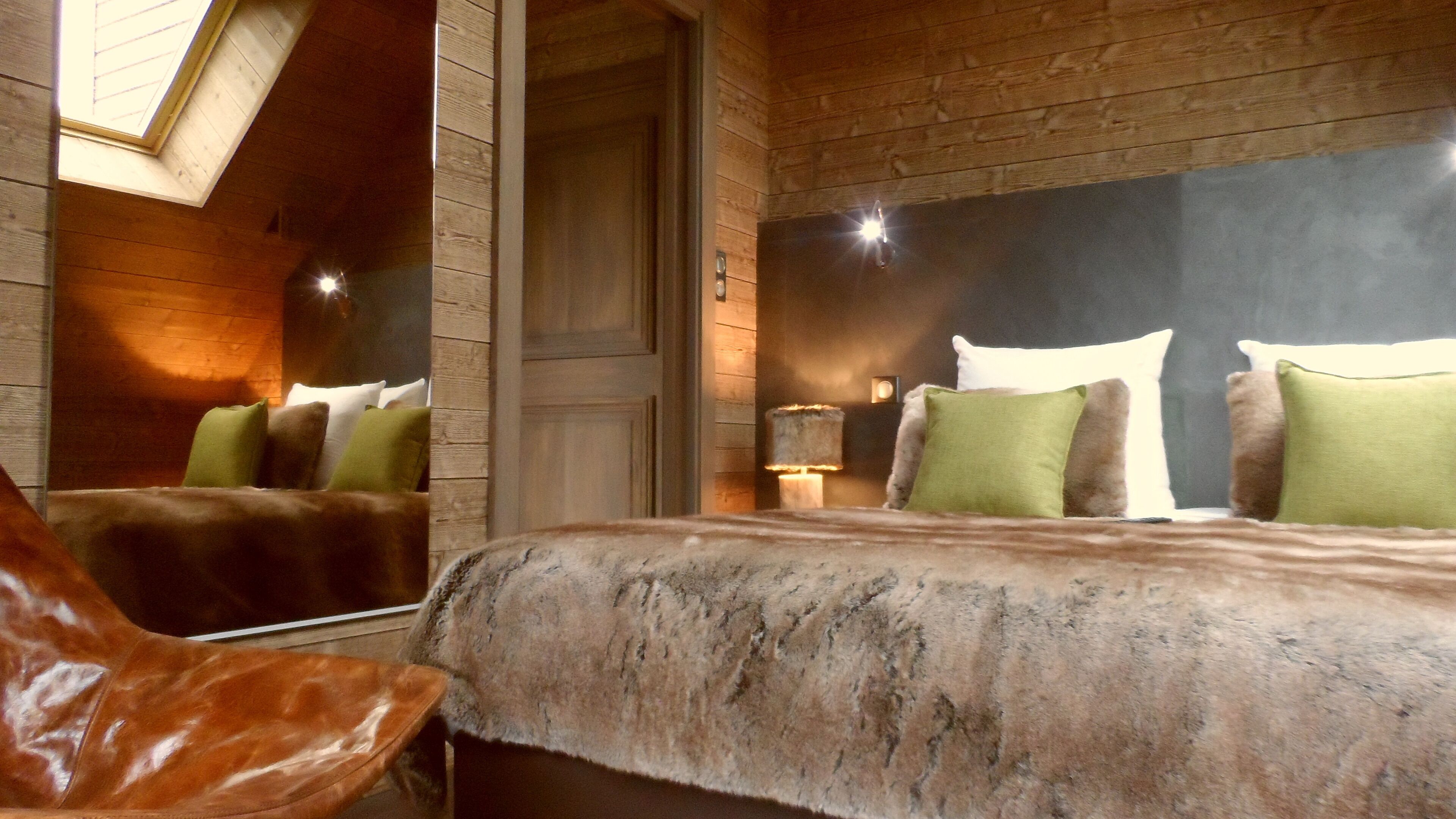 Una habitación acogedora con una cama grande, cabecero de madera, un espejo y un sillón de cuero.