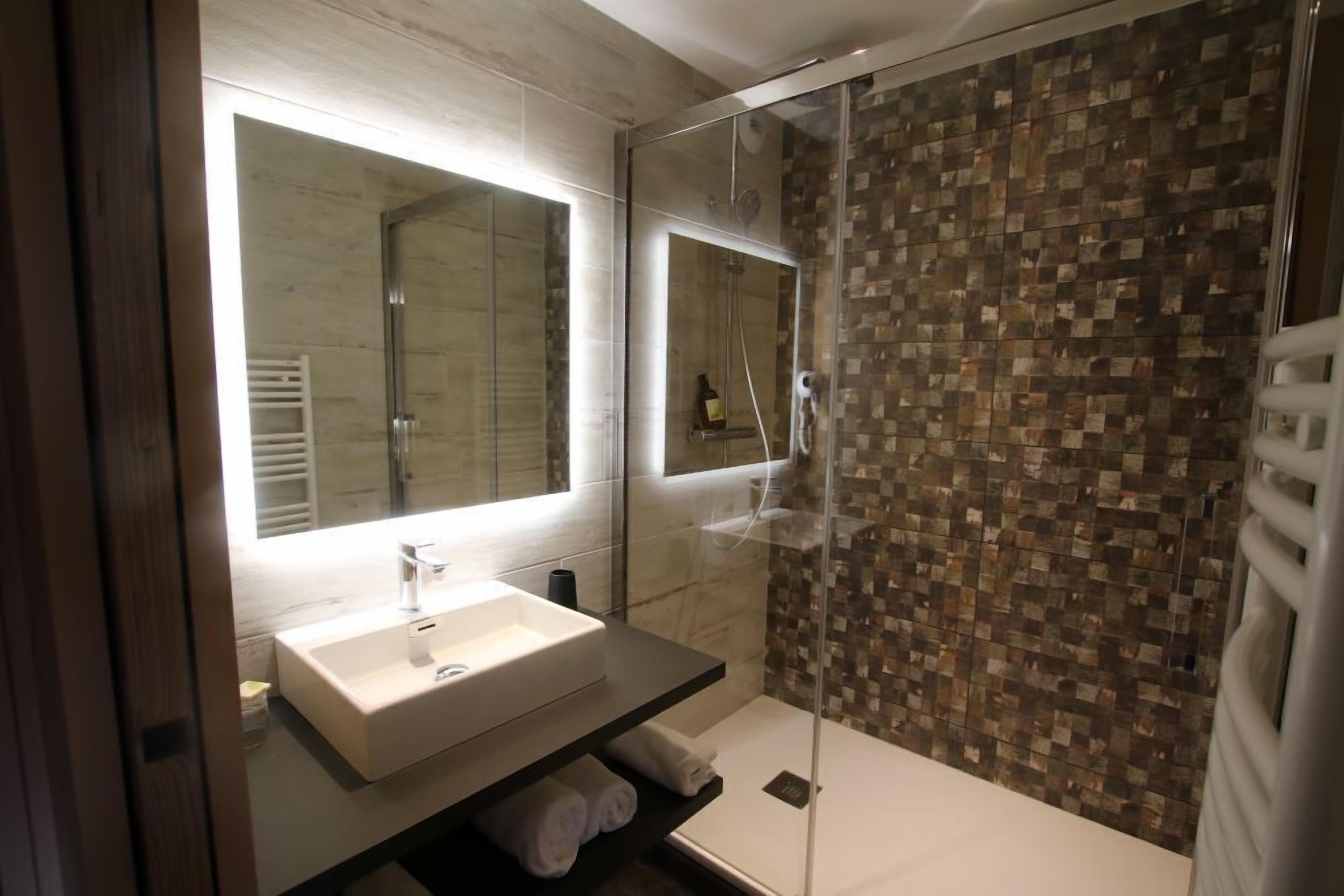 A modern bathroom with a glass-enclosed shower, a white sink, and a tiled shower wall.