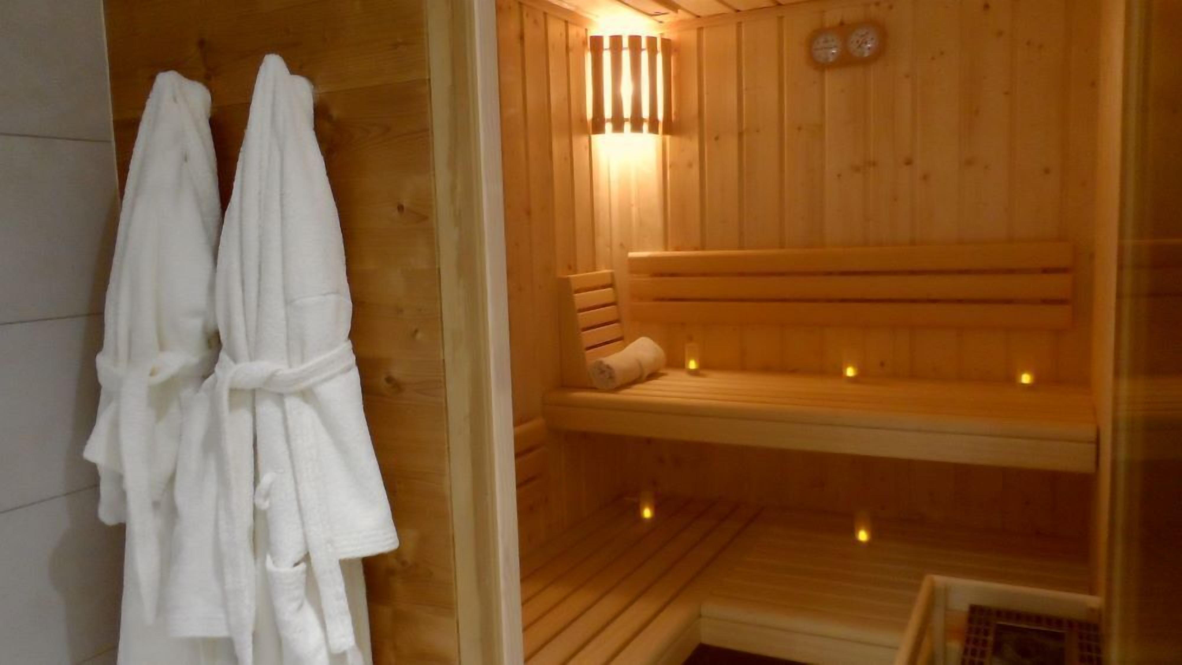 A wooden sauna with benches and a bench seat, and two white towels hanging on the wall.