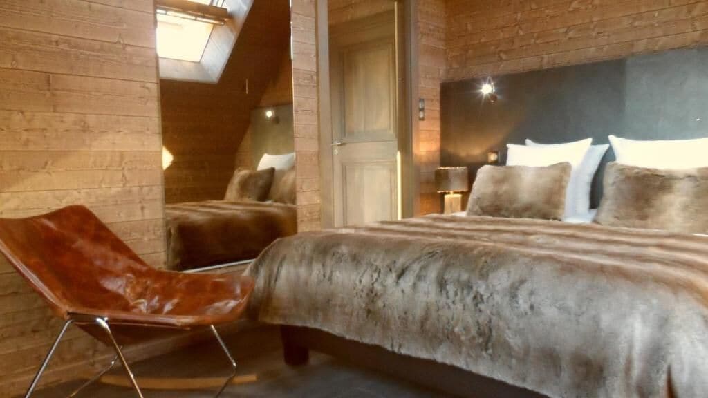 A bedroom with a large bed, a chair, and a wooden ceiling.