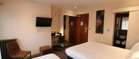 Habitación de hotel con dos camas, un escritorio, una silla, un televisor y un baño visible a través de una puerta abierta.
