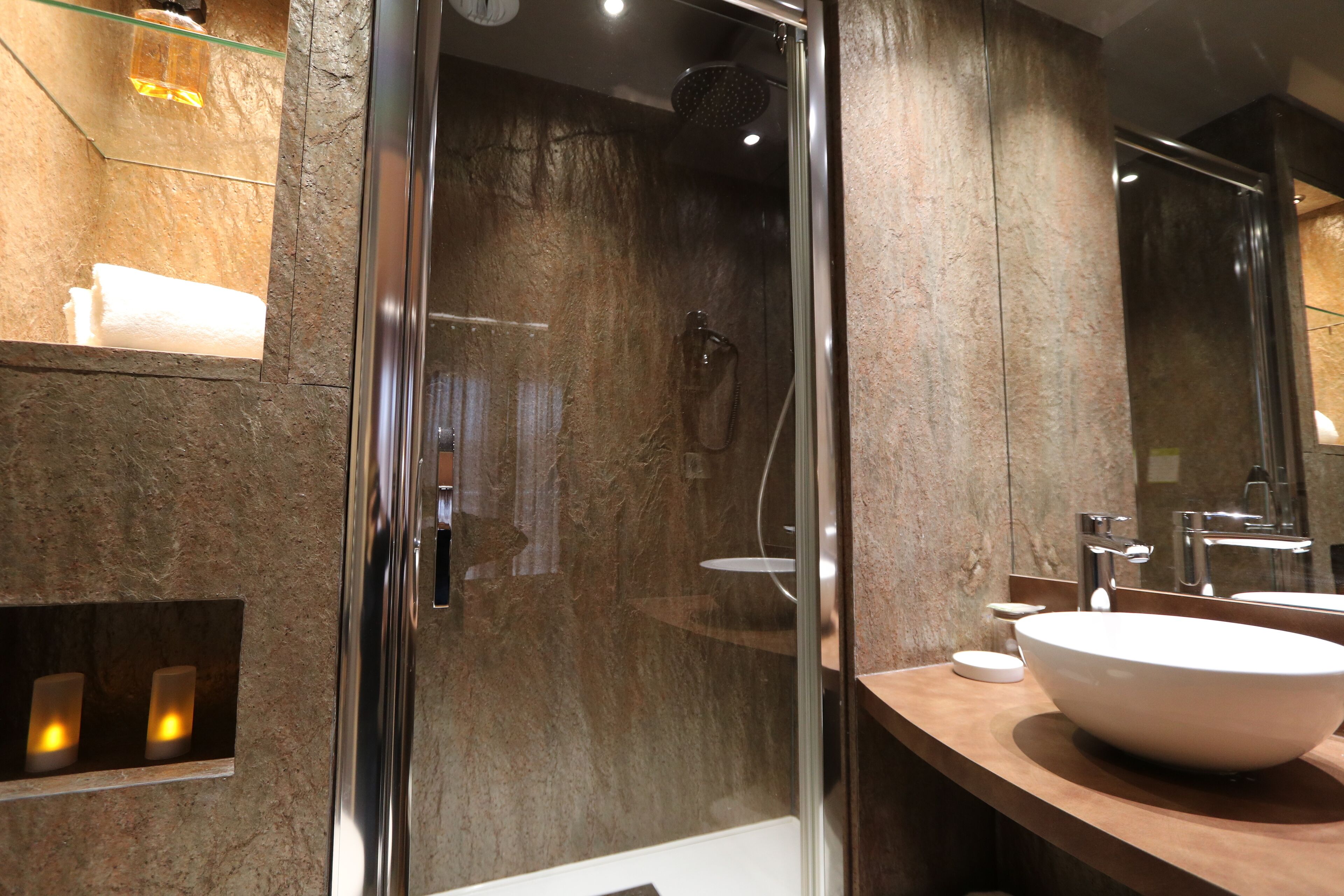 A modern bathroom with a glass-enclosed shower, a large white sink, and a marble wall.