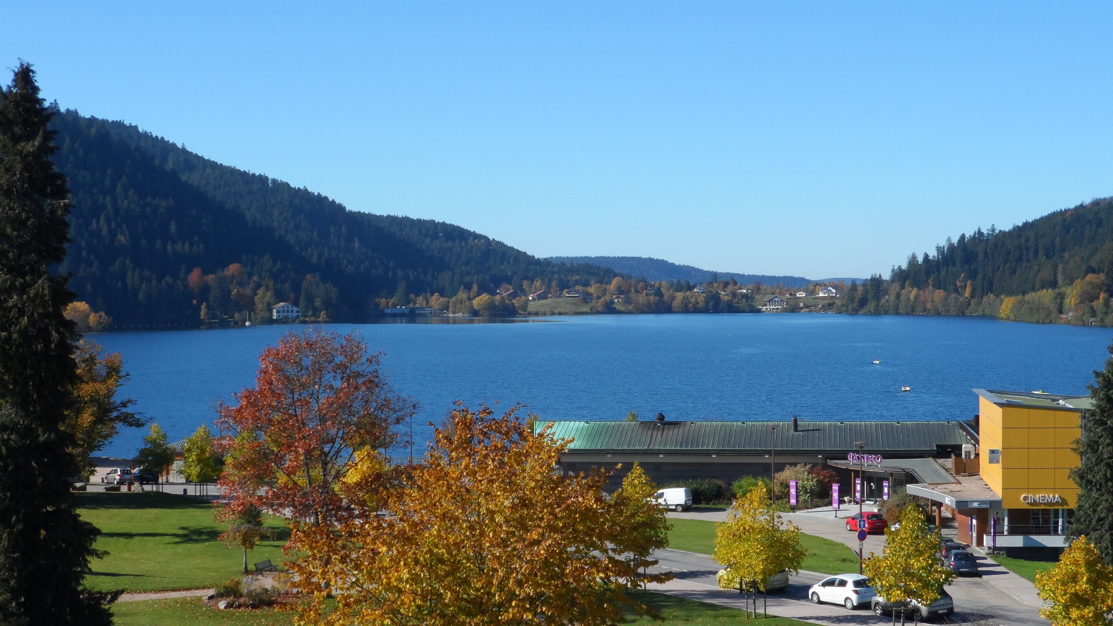 A lakeside view with a building labeled "CINEMA" in the foreground, surrounded by autumn foliage and a clear blue sky.
