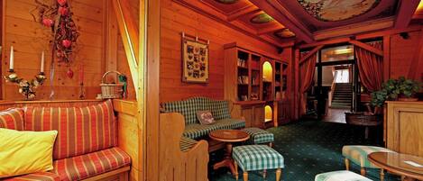 A cozy cabin interior with a wooden interior, a checkered sofa, a small table, and a bookshelf.