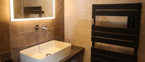 A modern bathroom with a large mirror, a white sink, and a towel rack.