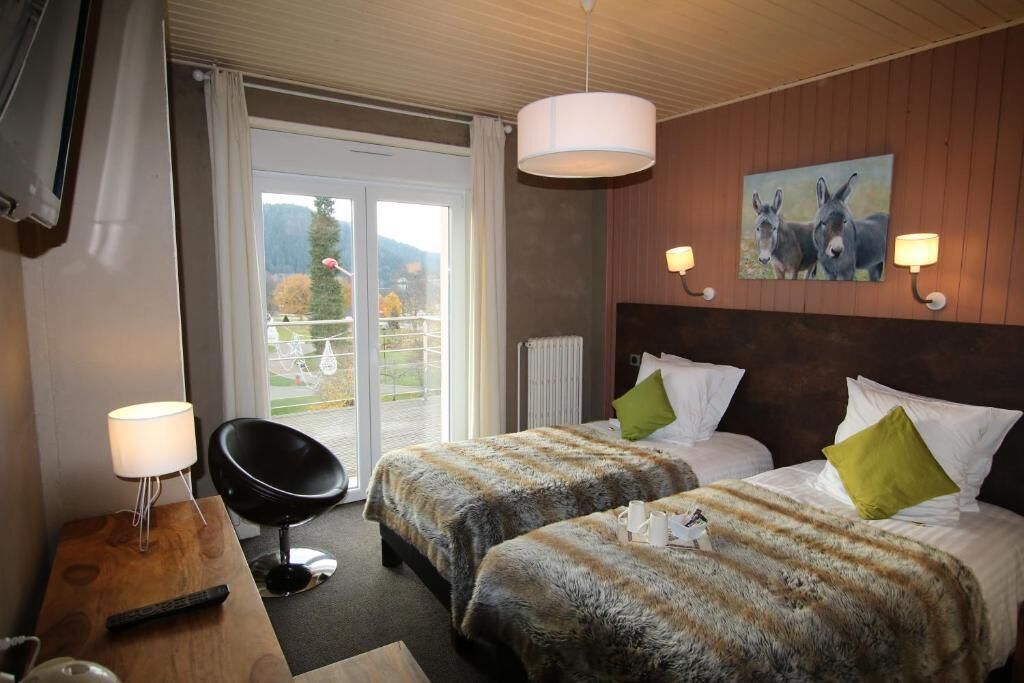 A hotel room with two beds, a wooden nightstand, a chair, and a large window with a view of the outdoors.