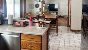 Una cocina con una isla central, armarios de madera, microondas integrado y una zona de comedor con televisión.