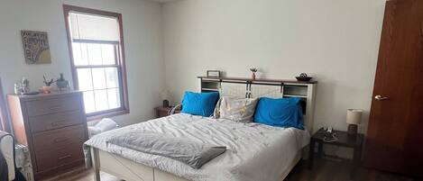 A bedroom with a bed, a ceiling fan, a window, a dresser, and a door.