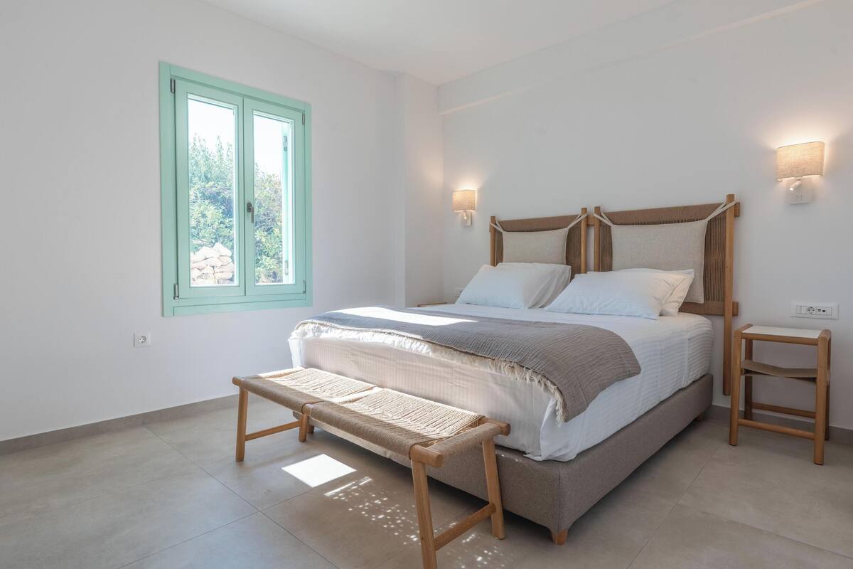Un dormitorio con cama, banqueta, mesitas de noche y ventana.