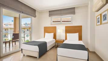Een hotelkamer met twee bedden, een raam met uitzicht op gebouwen, een lamp en een schuifdeur naar een buitenruimte.