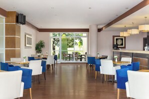 A modern hotel lobby with wooden flooring, blue and white chairs, a reception desk, and large windows offering a view of the outdoors. - Unique Residence Hotel Golf & Spa (Soke)