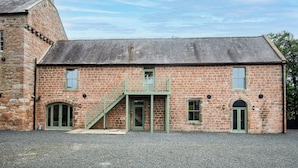 A stone building with a central entrance, a small balcony, and a gravel driveway.