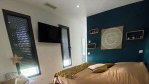 A modern bedroom with a bed, wooden floor, a TV mounted on the wall, and a window with blinds. - Superb villa with pool (Unknown)