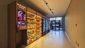 A hallway with vending machines stocked with snacks and beverages, leading to a glass door entrance. - Art Studio by VLV Stays (Salvador)