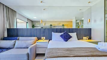 Quarto de hotel moderno com uma cama grande, duas mesas de cabeceira, um sofá e um espelho amplo.