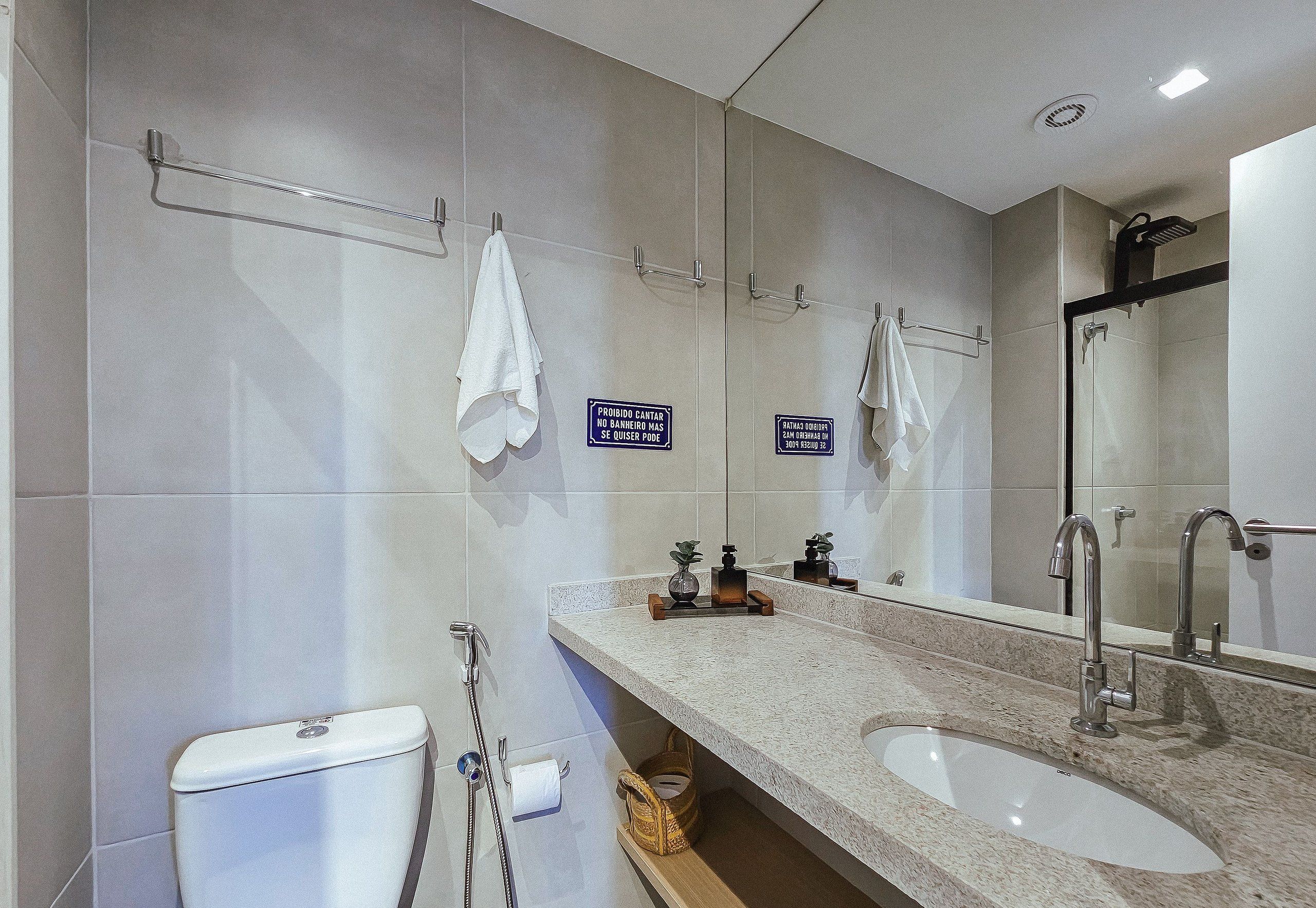 A modern bathroom with a large mirror, two sinks, and a toilet. There are towels hanging on hooks and a sign indicating no towel drying.