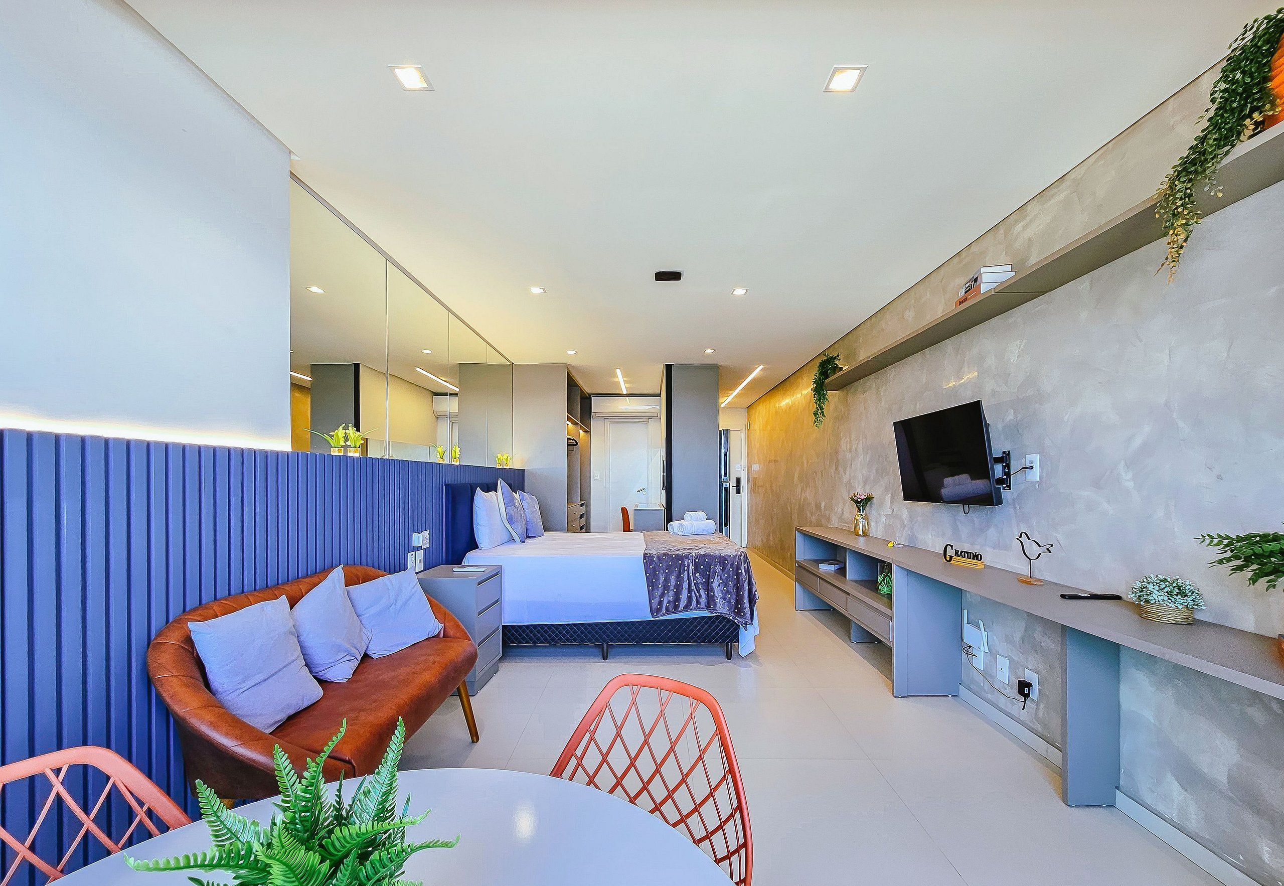 A modern hotel room with a bed, a sofa, a dining table, and a TV.