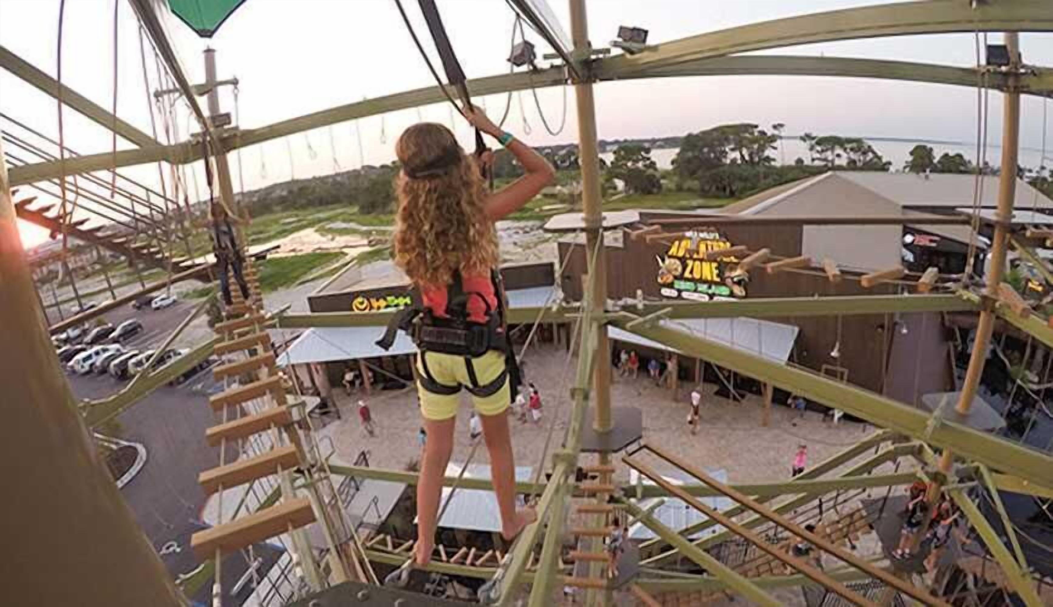 A person on a high platform with a safety harness, overlooking a park area with a sign that reads "Merry Go Round Zone".
