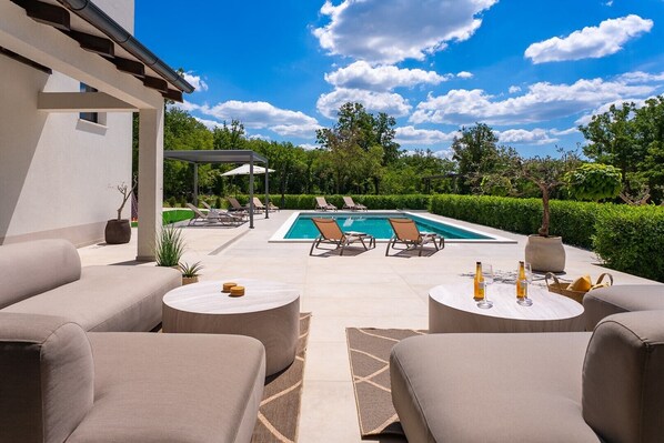 A poolside area with lounge chairs, a table, and a pergola.