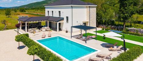 Ein modernes Haus mit Schwimmbad, Sitzgelegenheiten im Freien und einer überdachten Terrasse.